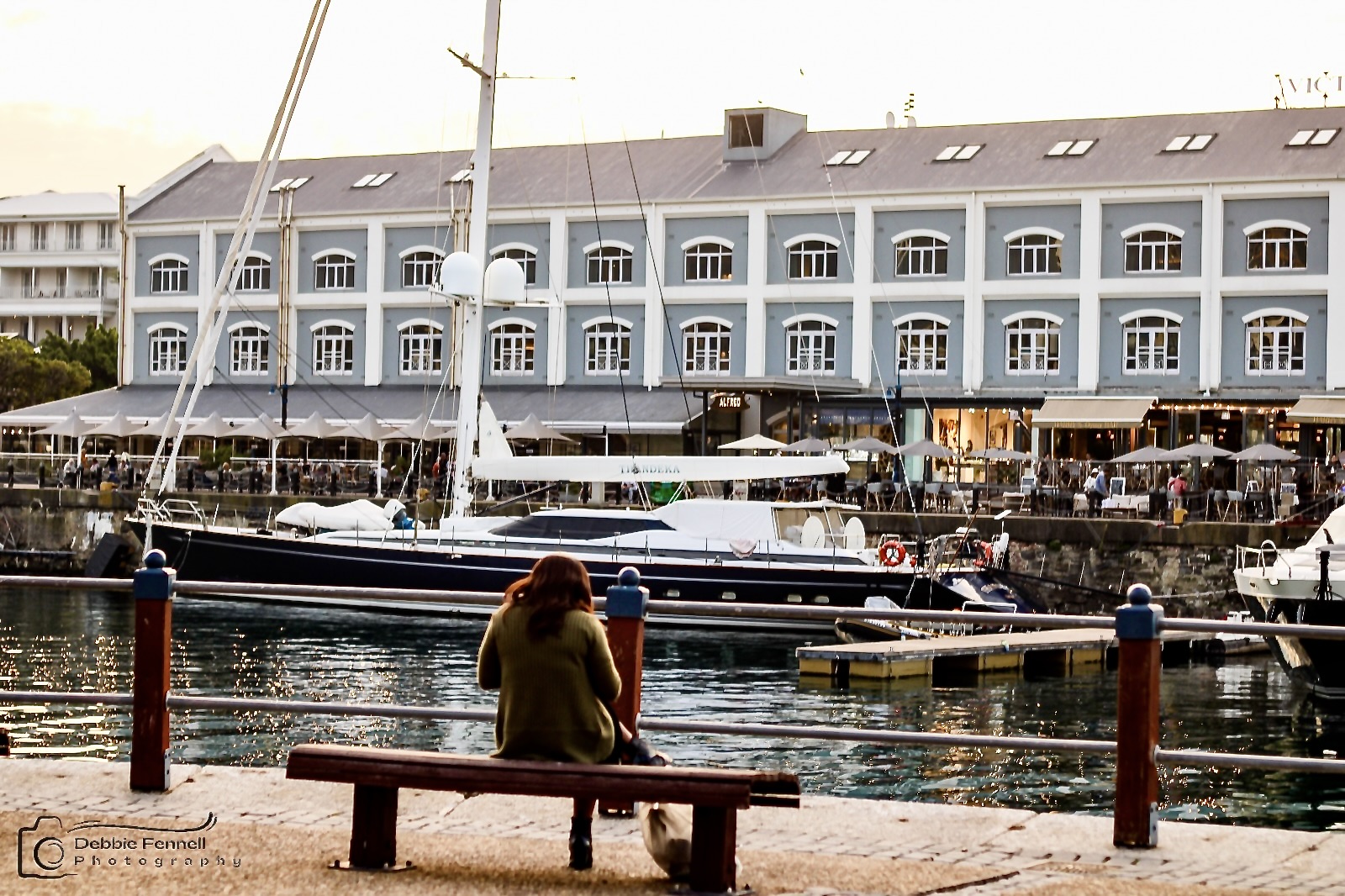 Victoria & Alfred Hotel viewed across the harbour, with moored yachts and a seated visitor in the foreground